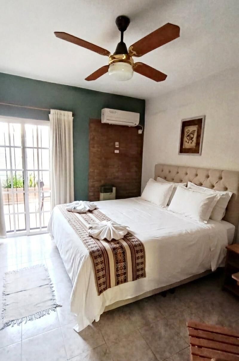 A bedroom with a bed, a ceiling fan, a window with curtains, and a wall-mounted air conditioner.