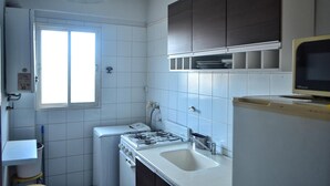 A compact kitchen with white tiles, a gas stove, a sink, and dark cabinets. - Torre los Platanos (San Miguel de Tucumán)