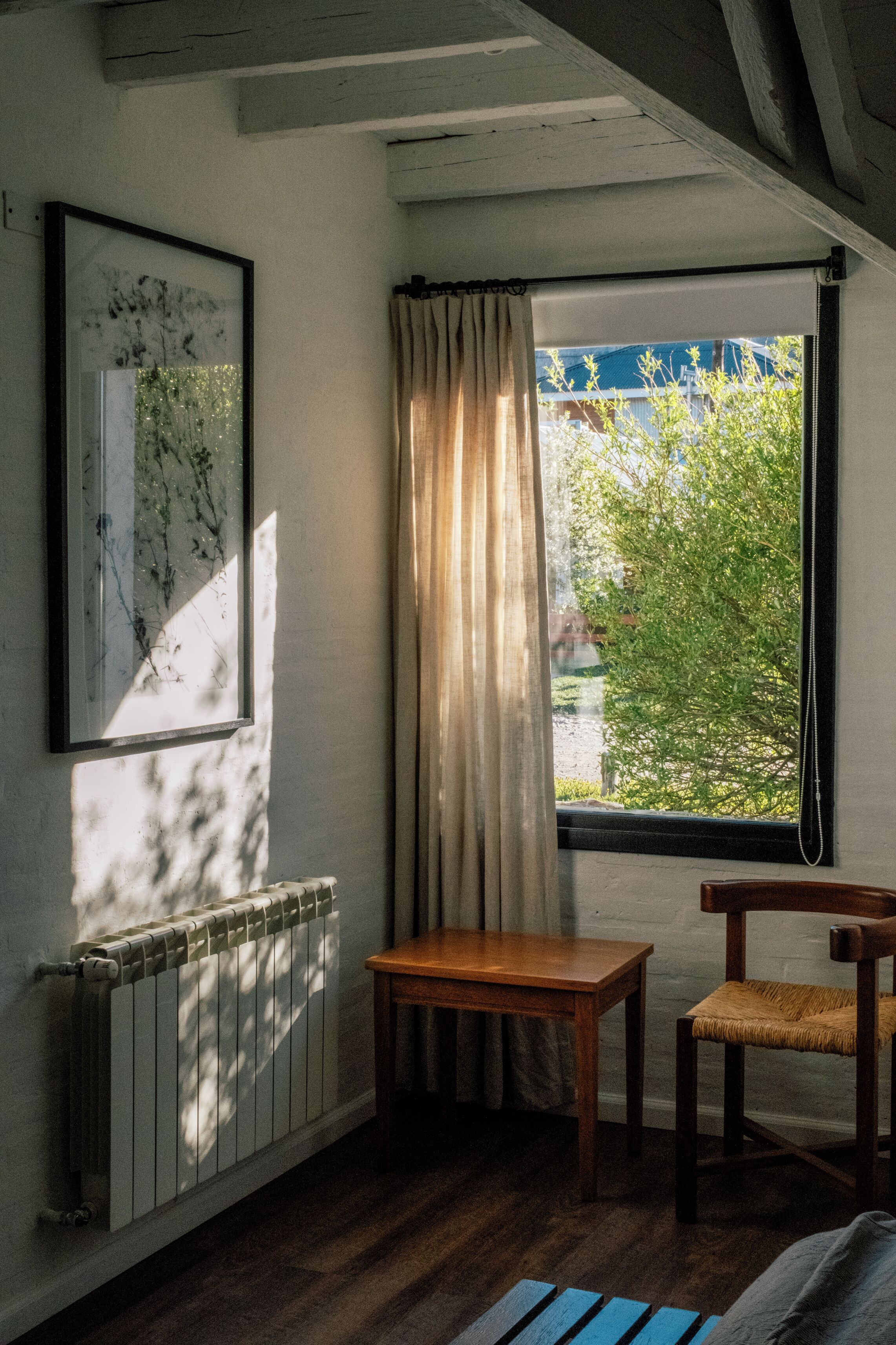 Una habitación con una mesa de madera, una silla, un radiador y un ventanal con cortinas.