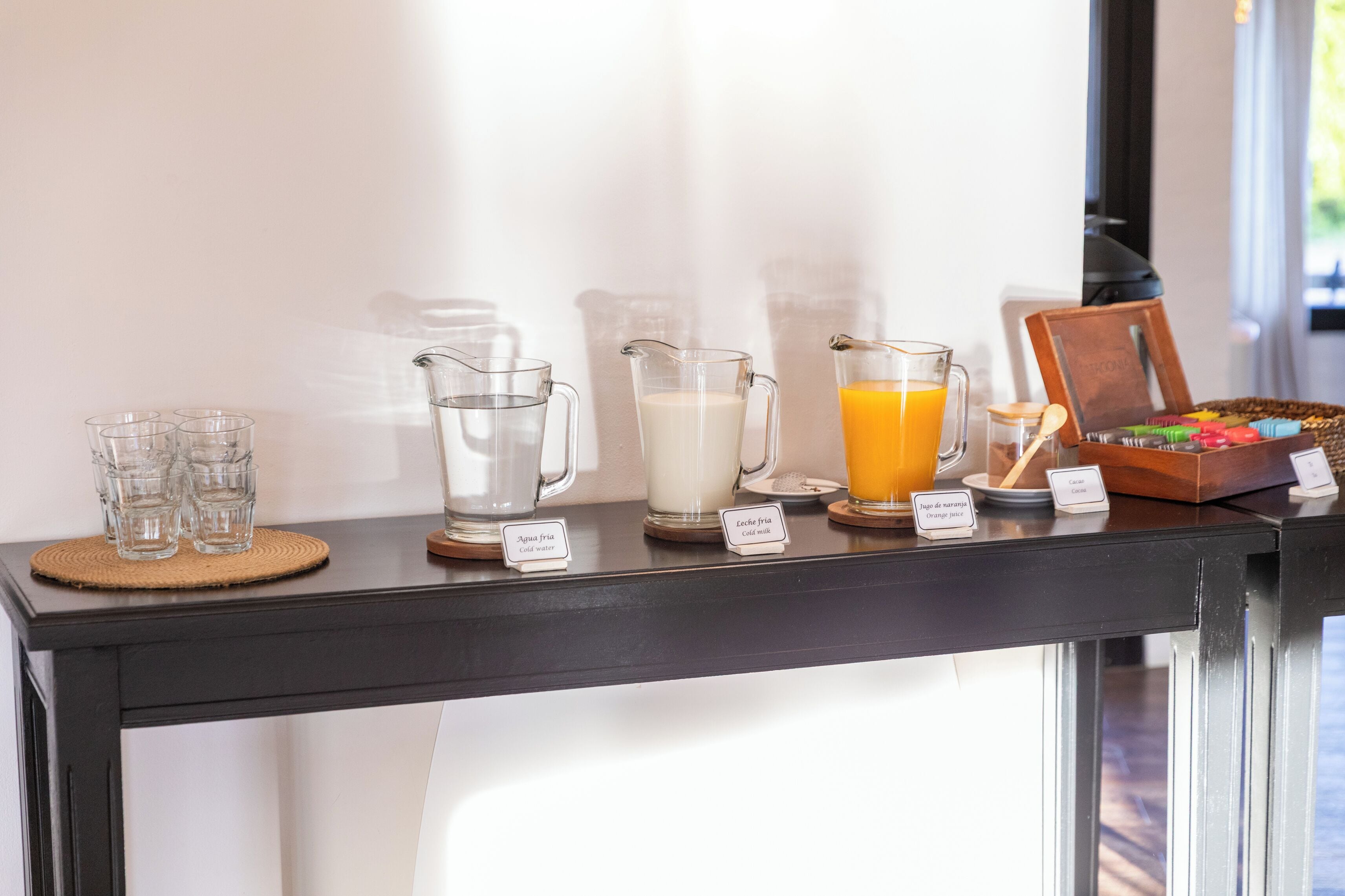 A beverage station with labeled pitchers of water, milk, and orange juice, and a basket of snacks.