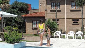 Una piscina con borde de azulejos, rodeada por una zona de patio con sillas de plástico blanco.