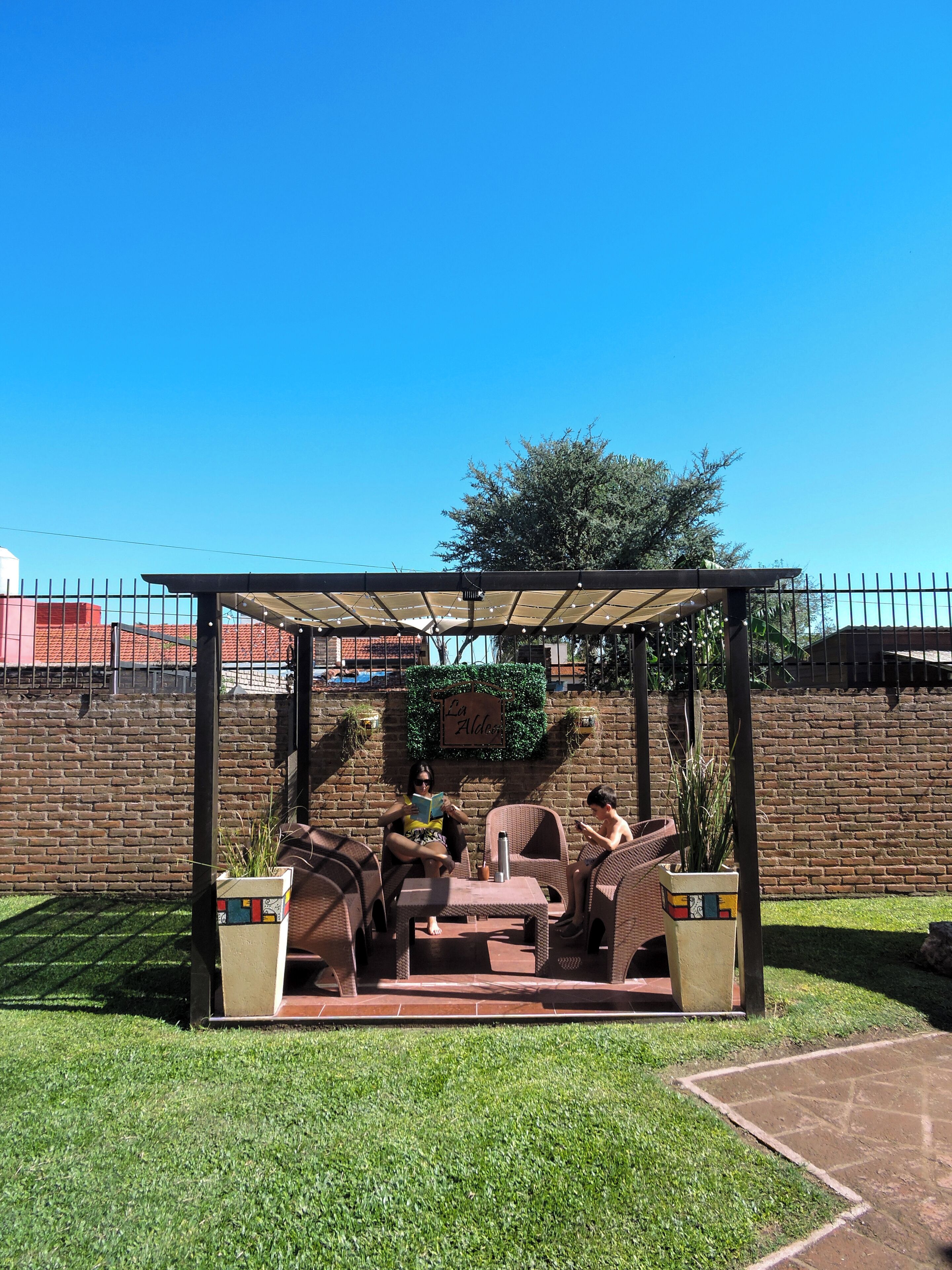 An outdoor seating area with a pergola, brick walls, and a clear blue sky.