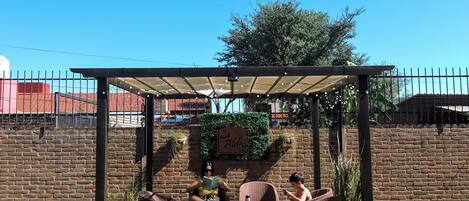 An outdoor seating area with a pergola, brick walls, and a clear blue sky.