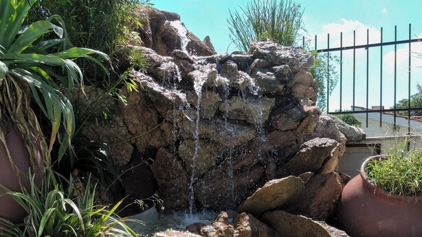 A rock waterfall feature surrounded by potted plants. - Cabañas la Aldea (Villa Carlos Paz)
