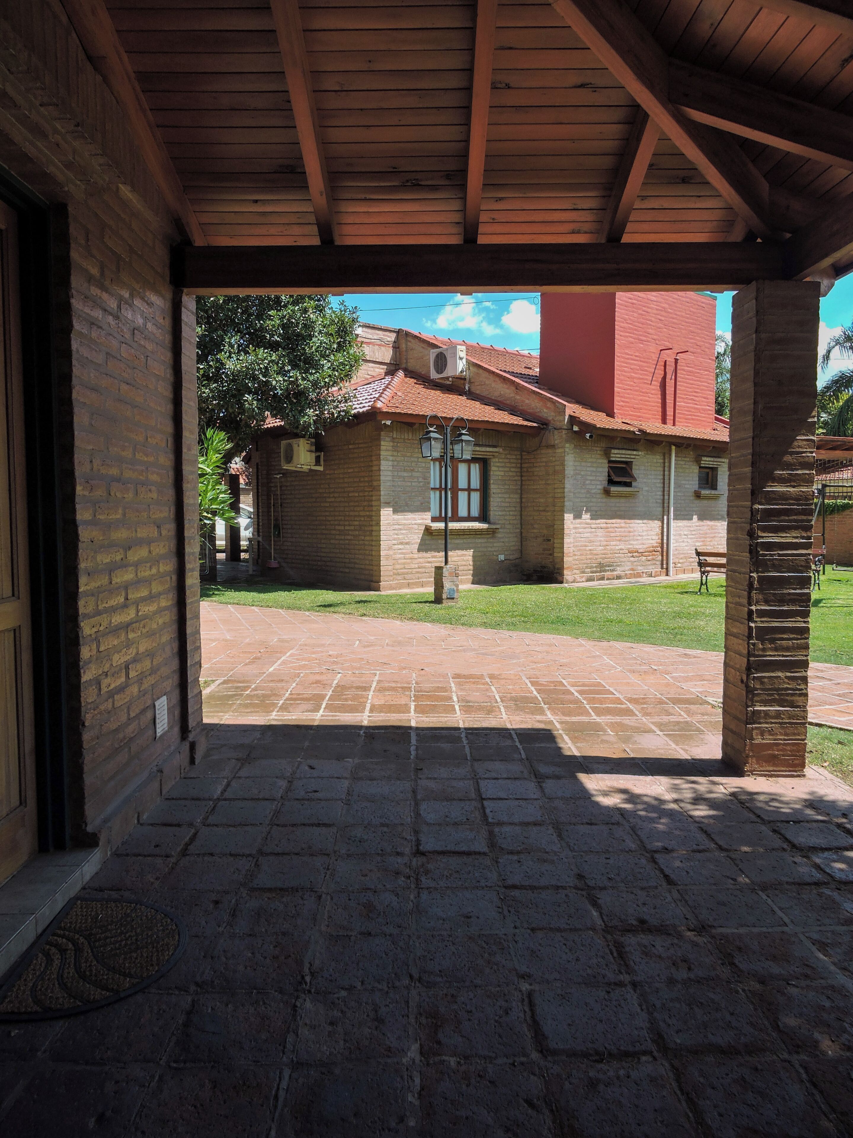 Un patio cubierto con suelo de ladrillo, techo de madera y vista a un edificio con techo rojo y una ventana.