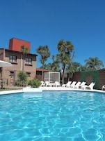 Una piscina al aire libre, sombrillas, sillones reclinables de piscina