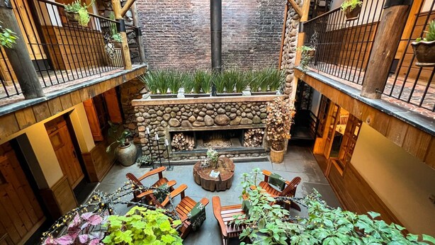 A cozy courtyard with a stone fireplace, wooden furniture, and potted plants. - Giardino di Pietra Hotel (Gramado)