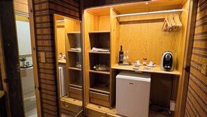 A compact, well-lit walk-in closet with wooden shelving, a small refrigerator, and a hanging rack. - Giardino di Pietra Hotel (Gramado)
