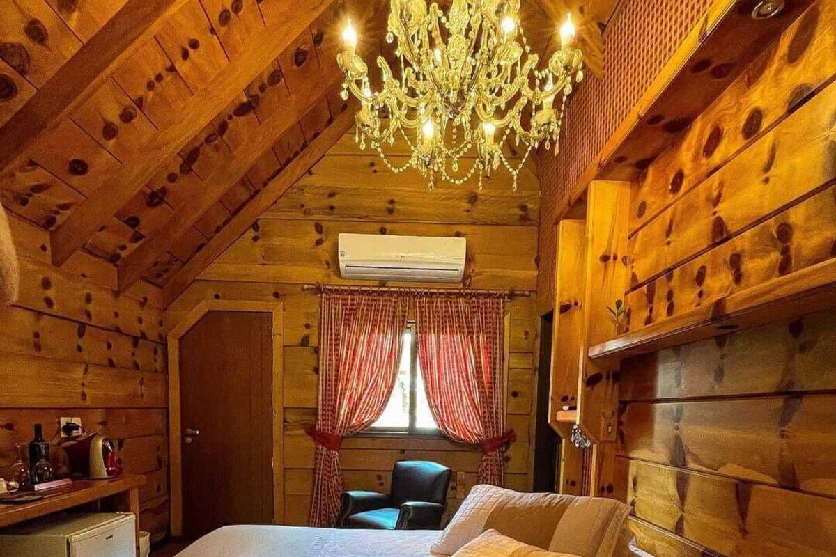 A cozy log cabin bedroom with a large bed, a chandelier, and a desk with a chair.