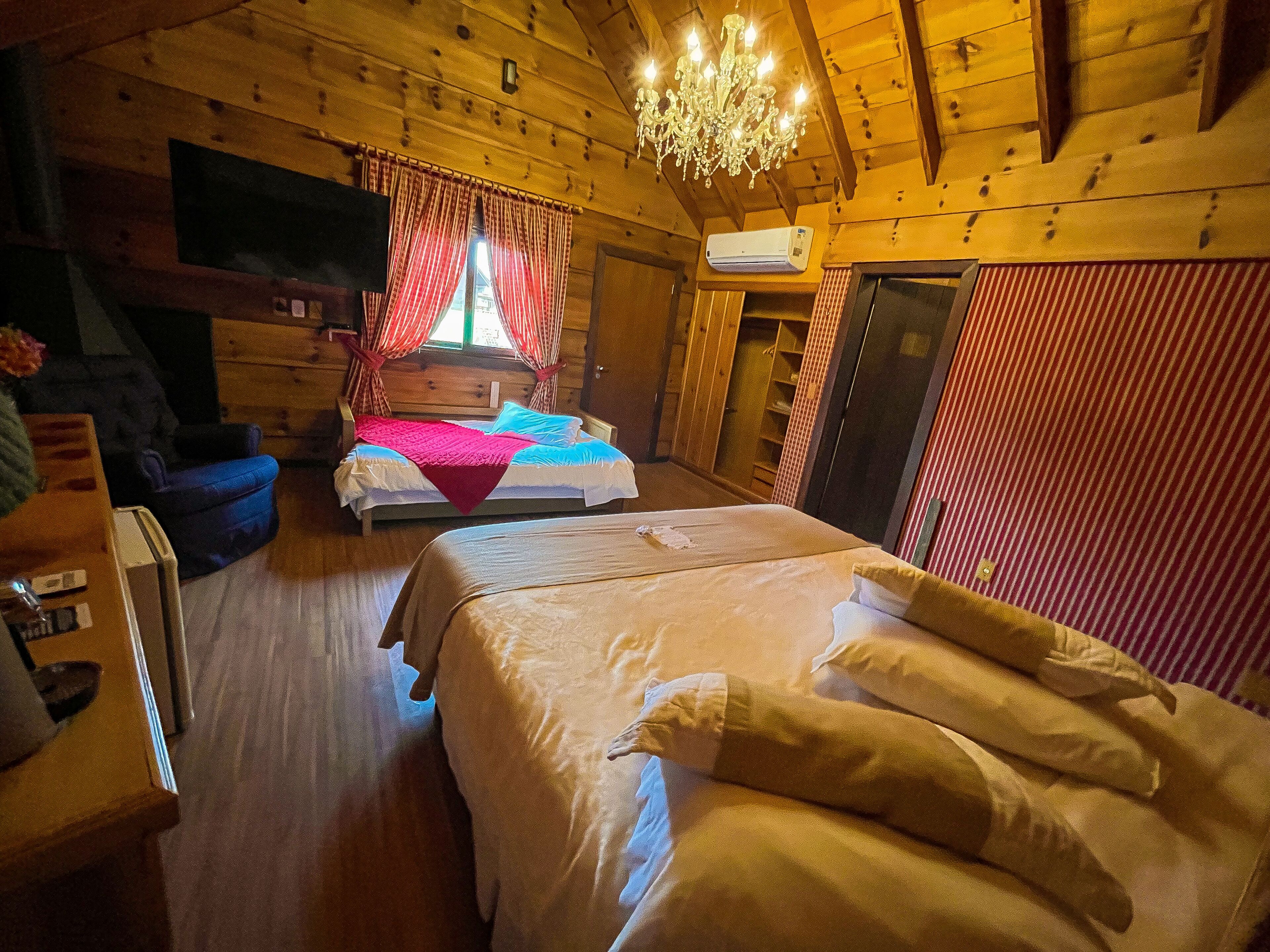 Une chambre confortable, aménagée dans le style d’un chalet, avec deux lits, un téléviseur et un lustre.