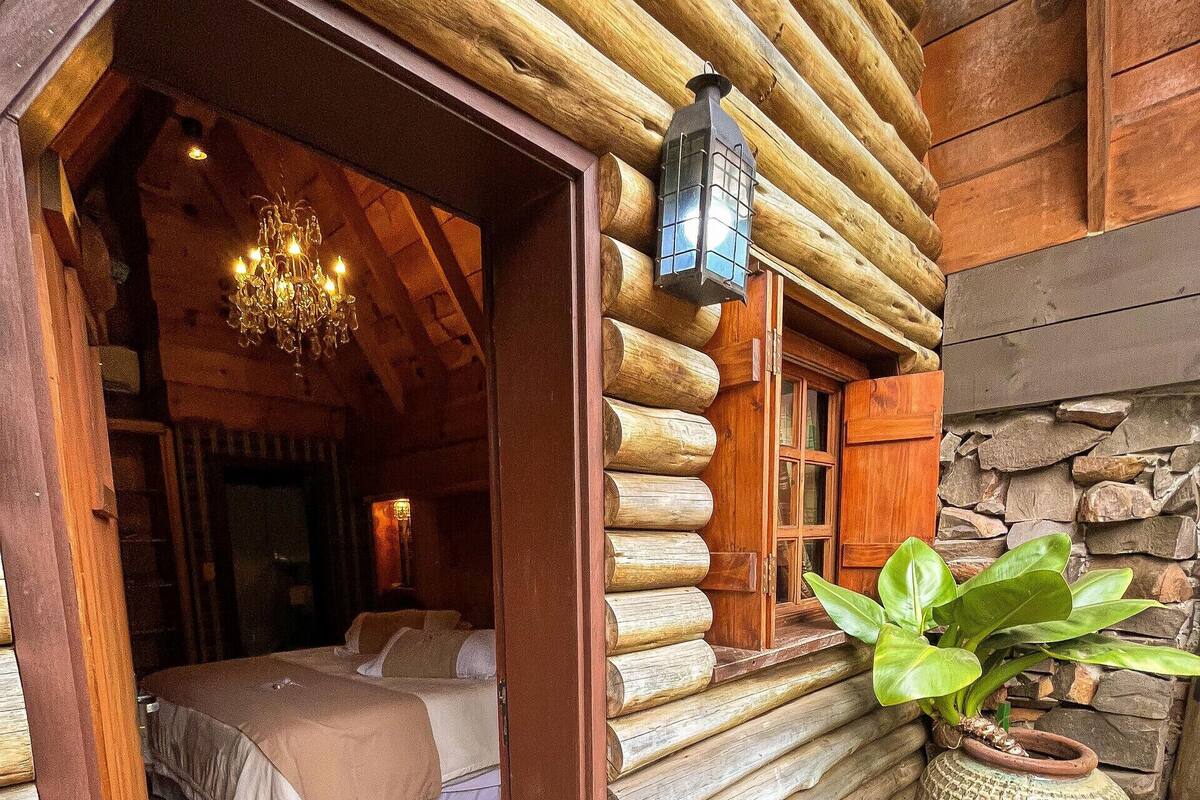 A log cabin room with a bed, a chandelier, a lantern, and a mosaic-tiled floor.