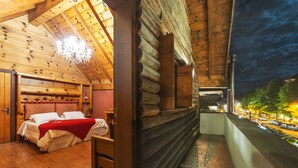 A log cabin room with a bed, wooden walls, a balcony with a view of the street, and a chandelier. - Giardino di Pietra Hotel (Gramado)