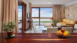 A room with a wooden table, a bowl of fruit, a potted plant, a sofa, and a view of the beach. - Altaplaya Apart de Mar (Mar Azul)