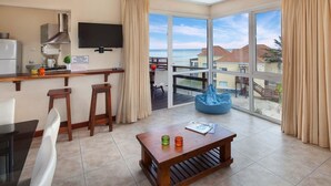 A modern hotel room with a kitchen area, a dining table, and a large balcony with a view of the sea and buildings. - Altaplaya Apart de Mar (Mar Azul)