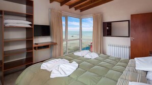 A bedroom with a bed, a TV, a wardrobe, and a view of the beach. - Altaplaya Apart de Mar (Mar Azul)