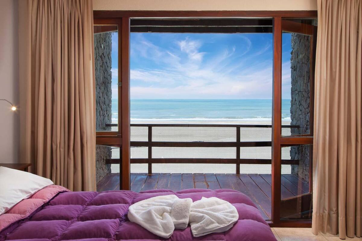 A bedroom with a bed, a view of the ocean, and a balcony with a railing.