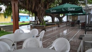 An outdoor patio area with white plastic chairs and tables, a green umbrella labeled 'Tona', and a stone bench. - Hotel Los Chilamates (Granada)