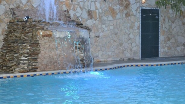 A stone wall with a waterfall feature and a pool with a tiled edge. - Hotel Los Chilamates (Granada)