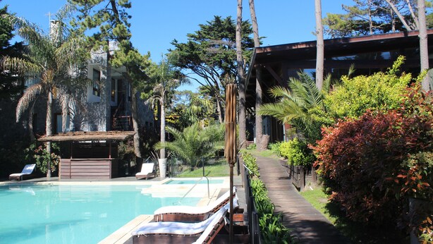 A pool area with lounge chairs, a wooden deck, and a building with a modern design.
