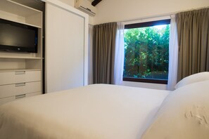 Ein Hotelzimmer mit Bett, Fernseher auf einem Tisch, Fenster mit Vorhängen und Blick auf Grünfläche.