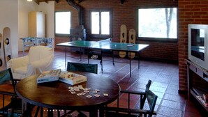 A room with a foosball table, a ping pong table, and a fireplace. There are chairs and a table with playing cards.