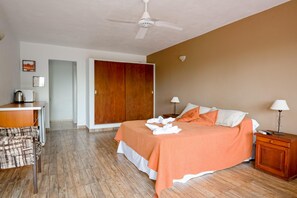 A hotel room with a bed, bedside tables, a desk, a chair, a wardrobe, and a ceiling fan.