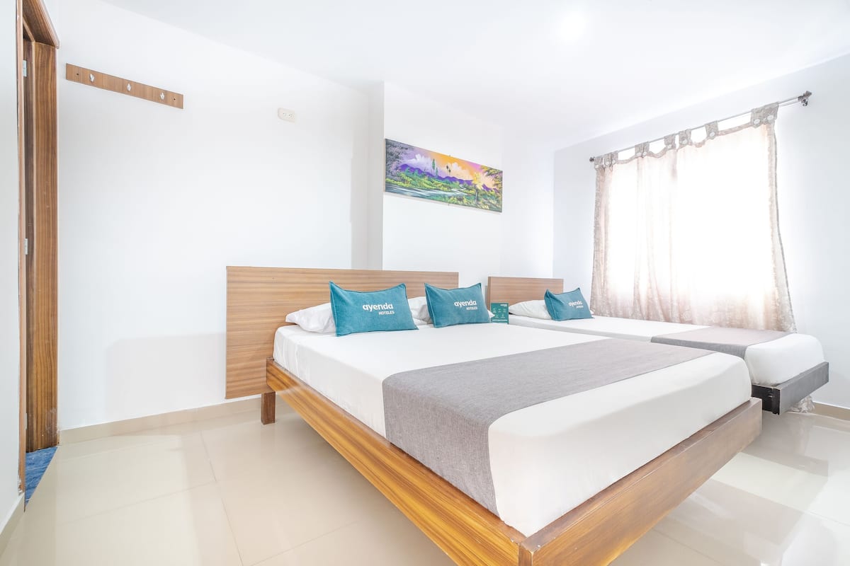 Une chambre d’hôtel avec un grand lit, un lit plus petit, une tête de lit en bois et un tableau au mur.