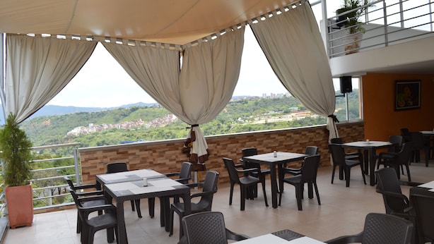 An outdoor dining area with tables and chairs, a view of a cityscape, and a balcony with a railing. - Ayenda 1501 Metropolitana Plaza (Bucaramanga)