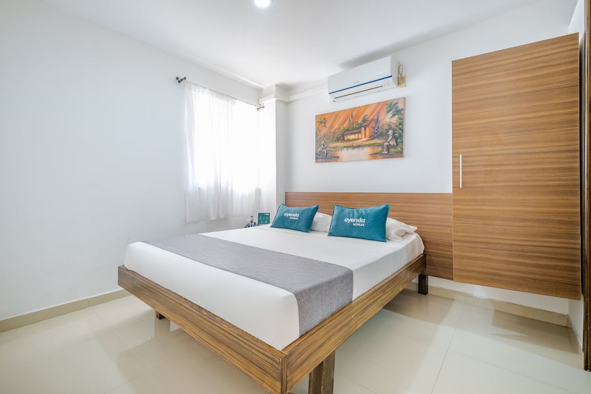 Une chambre d’hôtel moderne avec un cadre de lit en bois, du linge de lit blanc et des coussins de couleur turquoise.
