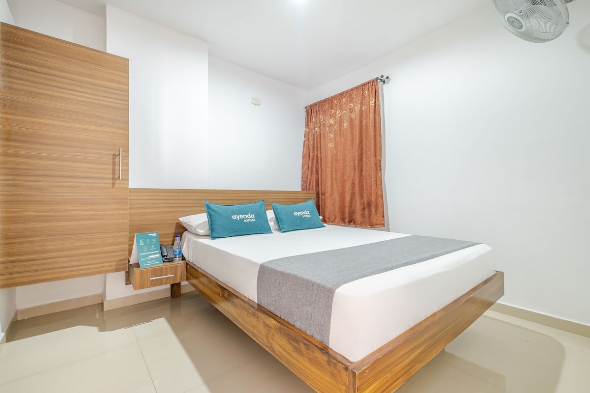 Une chambre d’hôtel moderne avec un lit en bois, une table de chevet avec une bouteille d’eau et un panneau indiquant les équipements disponibles.