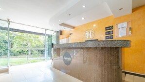 A hotel reception desk with a marble counter, a glass wall, and a view of greenery outside. - Ayenda 1501 Metropolitana Plaza (Bucaramanga)