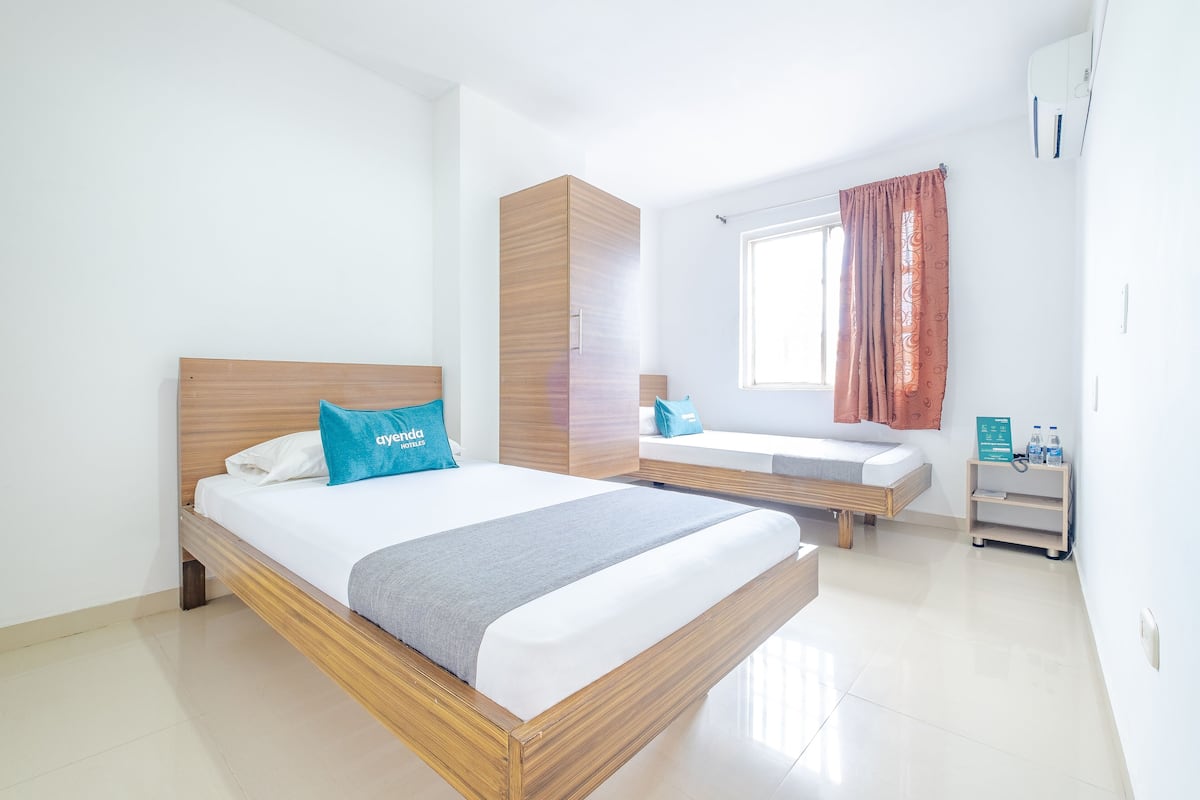 Une chambre d’hôtel moderne dotée d’un grand lit, d’une armoire intégrée, d’un petit coin salon et d’une fenêtre avec des rideaux.