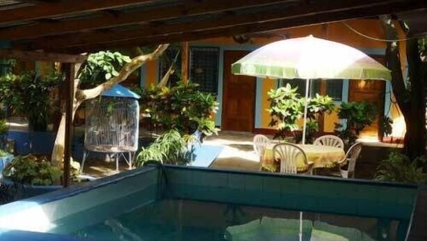 A covered outdoor area with a pool, chairs, and umbrellas. - Hotel Nicarao Inn (Rivas)