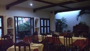 A restaurant with multiple tables and chairs, a high ceiling with exposed beams, and a view of the outdoors through large windows. - Hotel Nicarao Inn (Rivas)