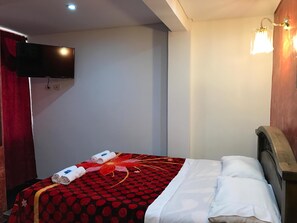 Una habitación de hotel con una cama, un televisor montado en la pared y una cortina roja.