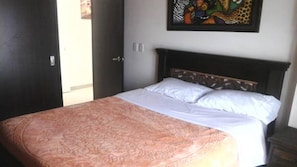 A bedroom with a bed, a door, and a wall with a framed picture.