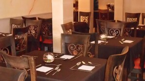 Un restaurante con varias mesas, cada una dispuesta con cubiertos y una copa. Las sillas tienen respaldos decorativos.
