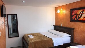 Una habitación de hotel con cama, mesita de noche, espejo y televisor montado en la pared.