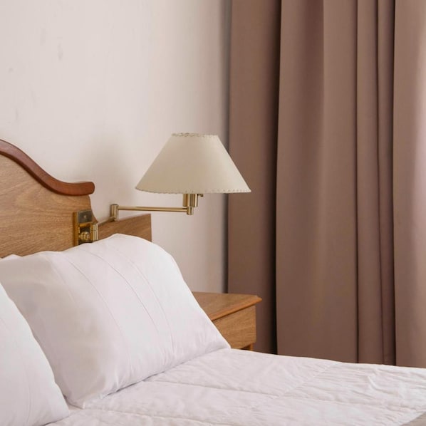 A hotel room with a bed, a nightstand, a lamp, and curtains.
