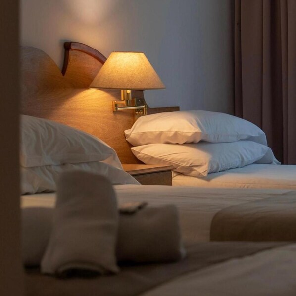 A neatly made bed with white linens and pillows, a bedside table with a lamp, and a wooden headboard. - Hotel Pinamar Soleado (Ostende)