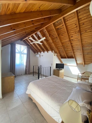 A bedroom with a sloped ceiling, a bed, a television, a chair, and a window. - Hotel Pinamar Soleado (Ostende)