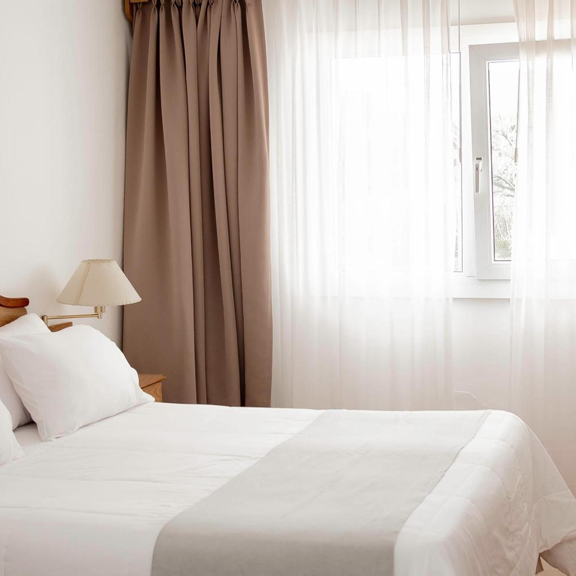 Ein Hotelzimmer mit einem Bett, einem Nachttisch, einer Lampe und durchsichtigen Vorhängen.