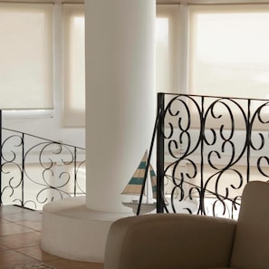 A spacious indoor area with a white column, a metal railing with intricate designs, and a view through large windows.