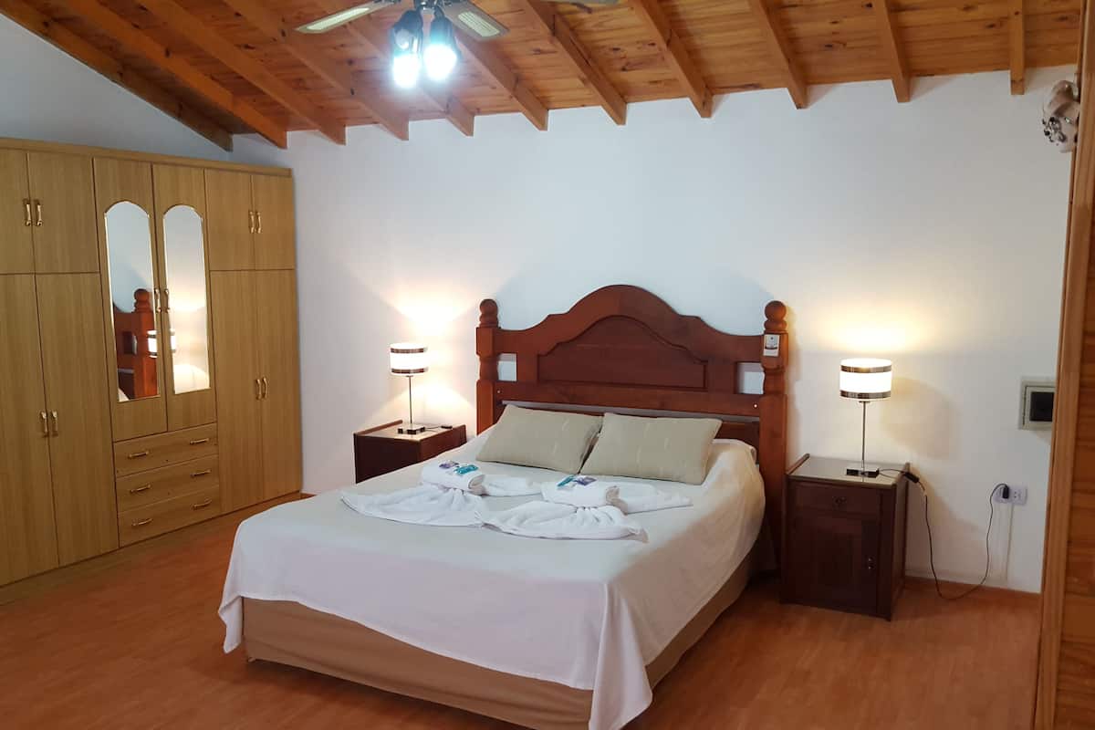 Un dormitorio con una cama de madera, dos mesitas de noche con lámparas, un armario de madera y un ventilador de techo.