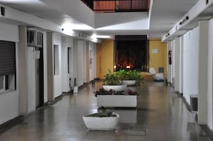 Un pasillo con paredes blancas, piso de baldosas y plantas en macetas.