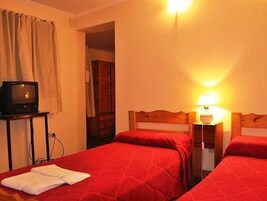 A hotel room with two beds, a television on a small table, and a lamp on a bedside table.
