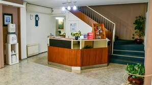 A reception area with a wooden desk, a clock, a radiator, and a staircase. - Nuevo City Hotel (Rosario)