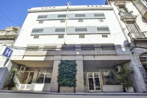 Un edificio de varios pisos con una entrada destacada, un llamativo muro verde y un letrero con la letra 'H' que indica un hospital.
