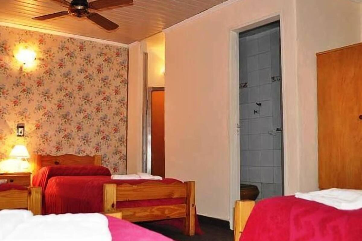 A room with two wooden beds, a ceiling fan, floral wallpaper, and a door.