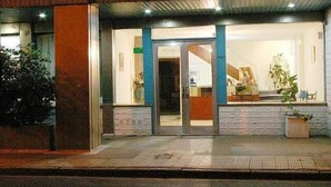 A building with a glass entrance, a wooden facade, and a small outdoor seating area with plants. - Nuevo City Hotel (Rosario)